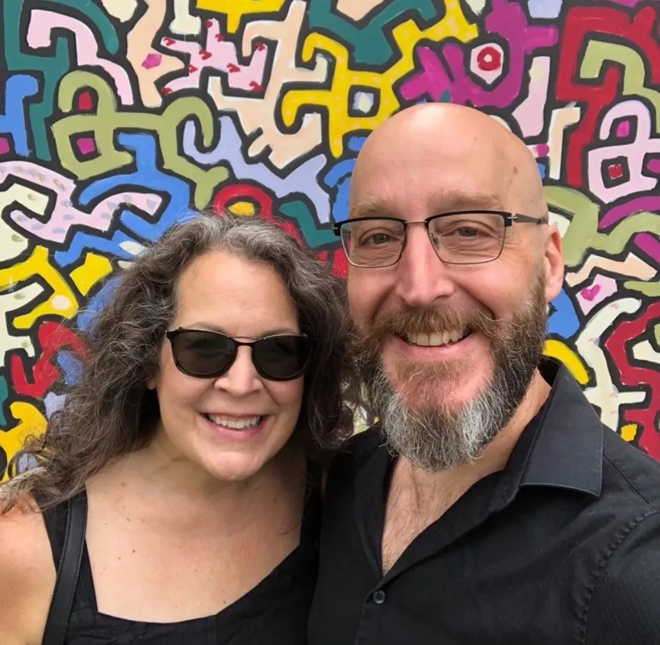 Wendy and Scott smiling in front of some multi-colored, geometric street art.