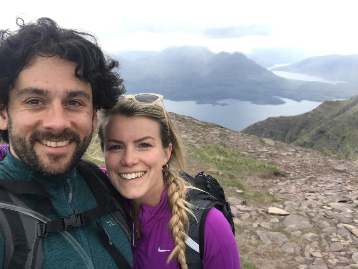 James and Aimee stood smiling in front of a scenic background