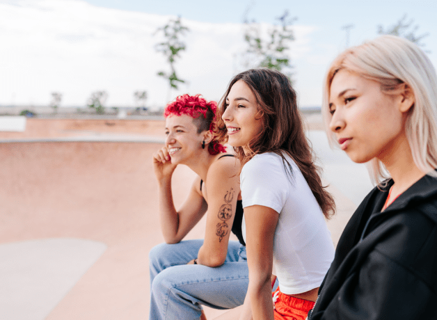 Three women sitting together at a skate park, staring into the distance.