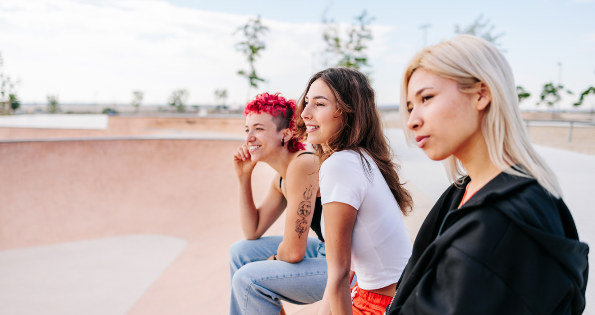 Three women sitting together at a skate park, staring into the distance.